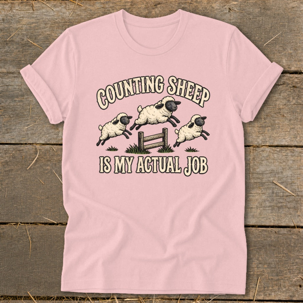 Pink t-shirt with cartoon sheep jumping over a fence and text "COUNTING SHEEP IS MY ACTUAL JOB".