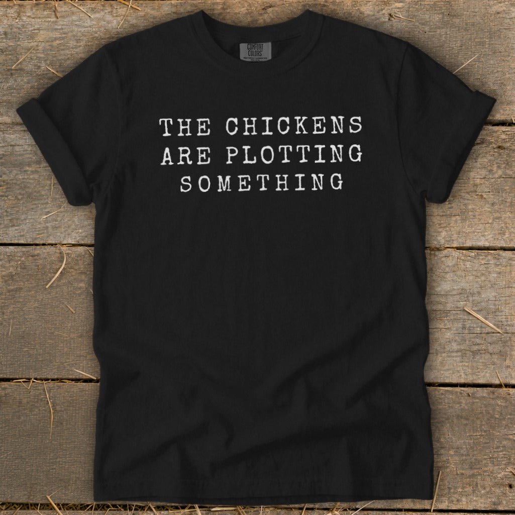 Black t-shirt with white text that reads "THE CHICKENS ARE PLOTTING SOMETHING".