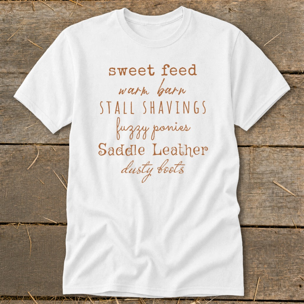 White t-shirt with text: sweet feed, warm barn, stall shavings, fuzzy ponies, saddle leather, dusty boots.