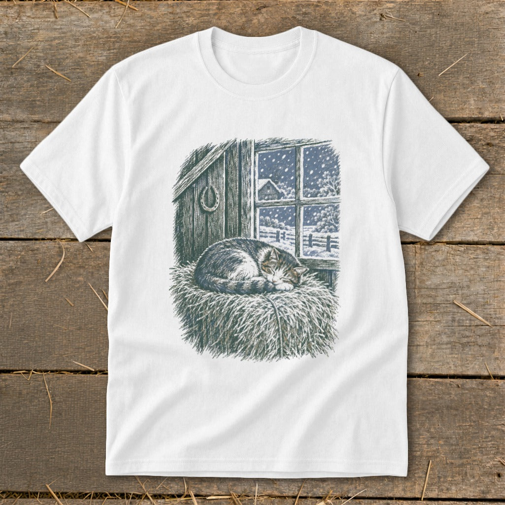 T-shirt graphic of a cat sleeping on hay in a barn with a snowy window view.