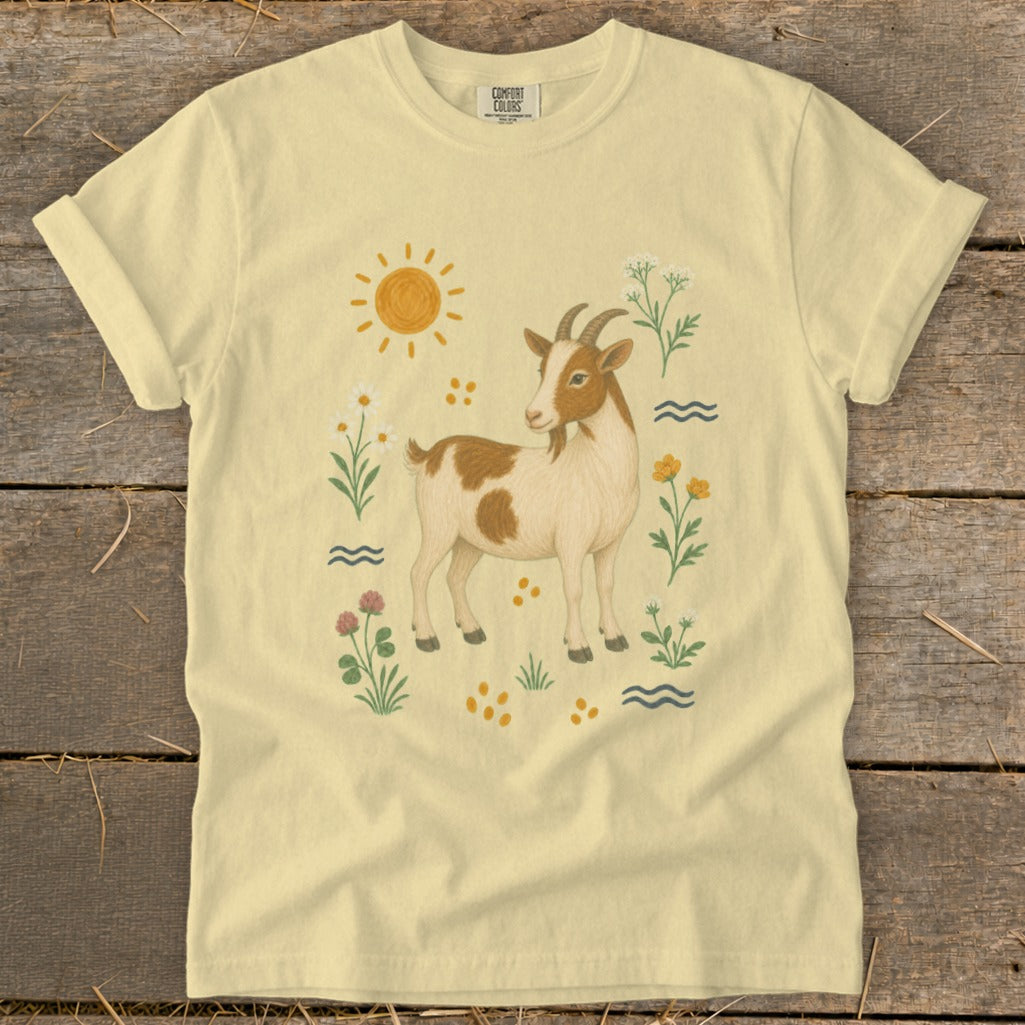 Light yellow t-shirt with a brown and white goat, sun, and flowers illustration.