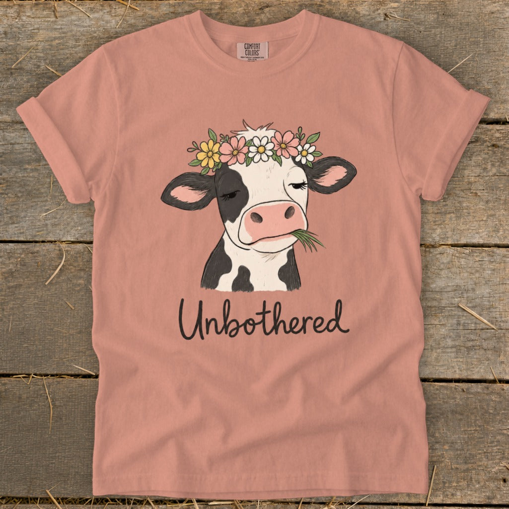 Illustration of cow with flower crown eating grass, with text "Unbothered" on t-shirt.