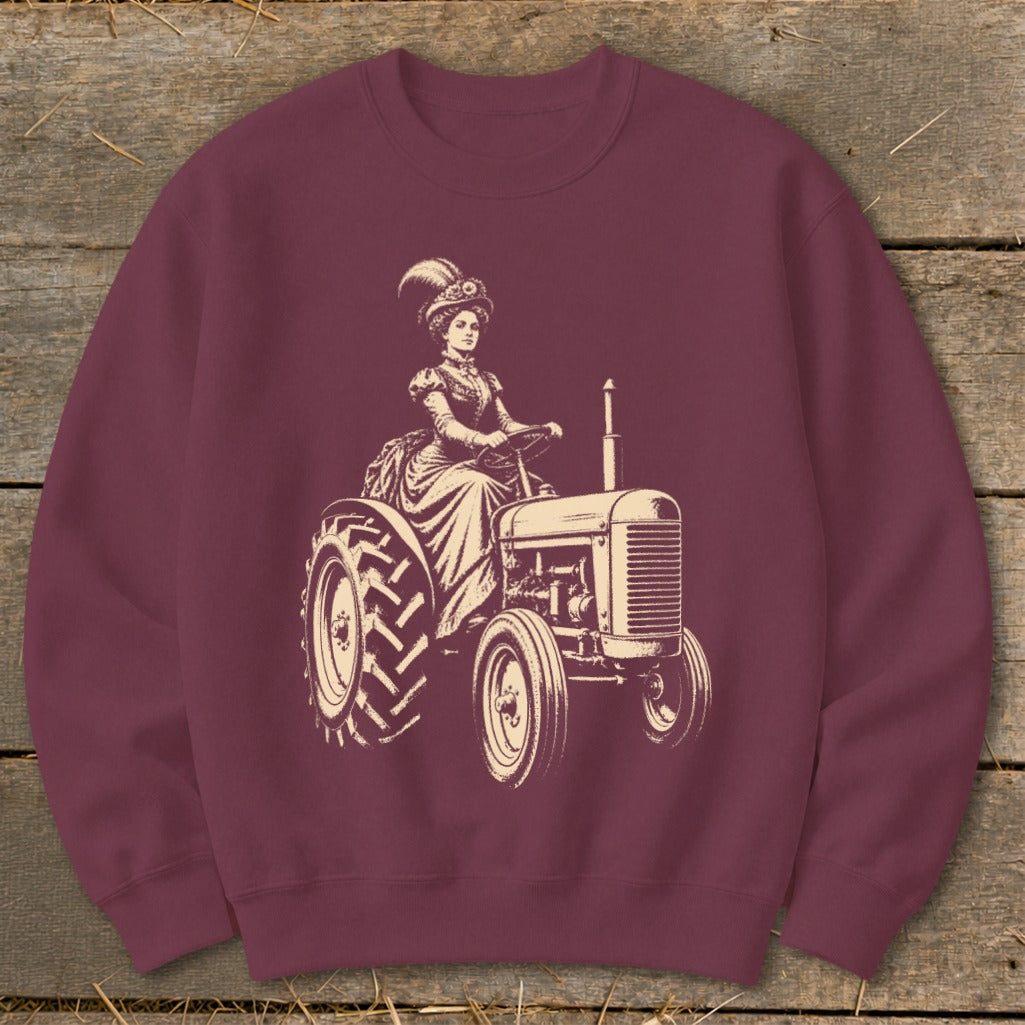 Vintage woman in ornate hat and dress driving a tractor on maroon sweatshirt.
