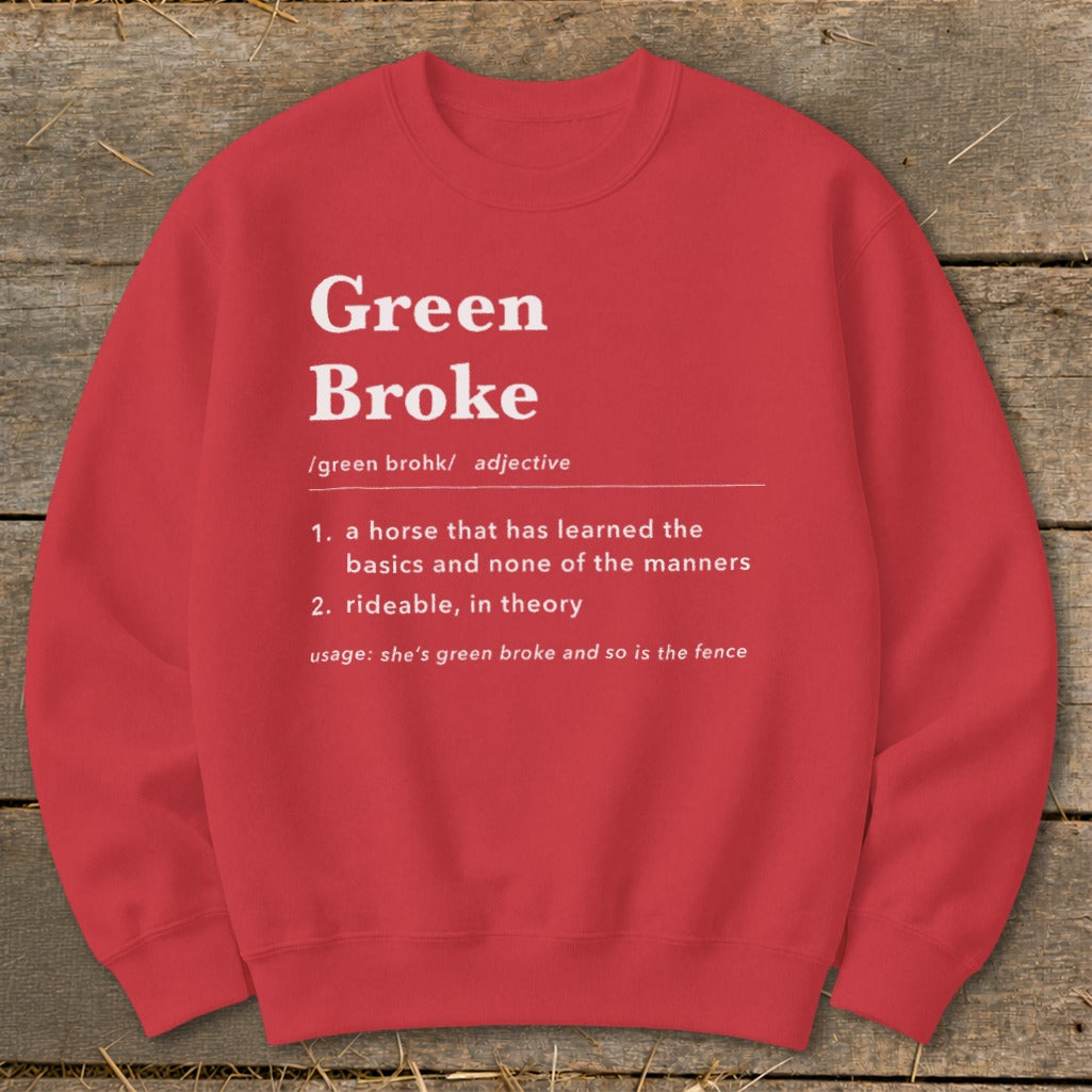 Red crewneck sweatshirt with white text defining "Green Broke" laid on a wooden surface.