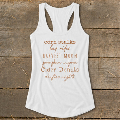 White tank top with text listing fall activities: corn stalks, hay rides, harvest moon, pumpkin wagons, cider donuts, bonfire nights.