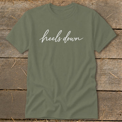 Olive green t-shirt with white script text that reads "heels down."