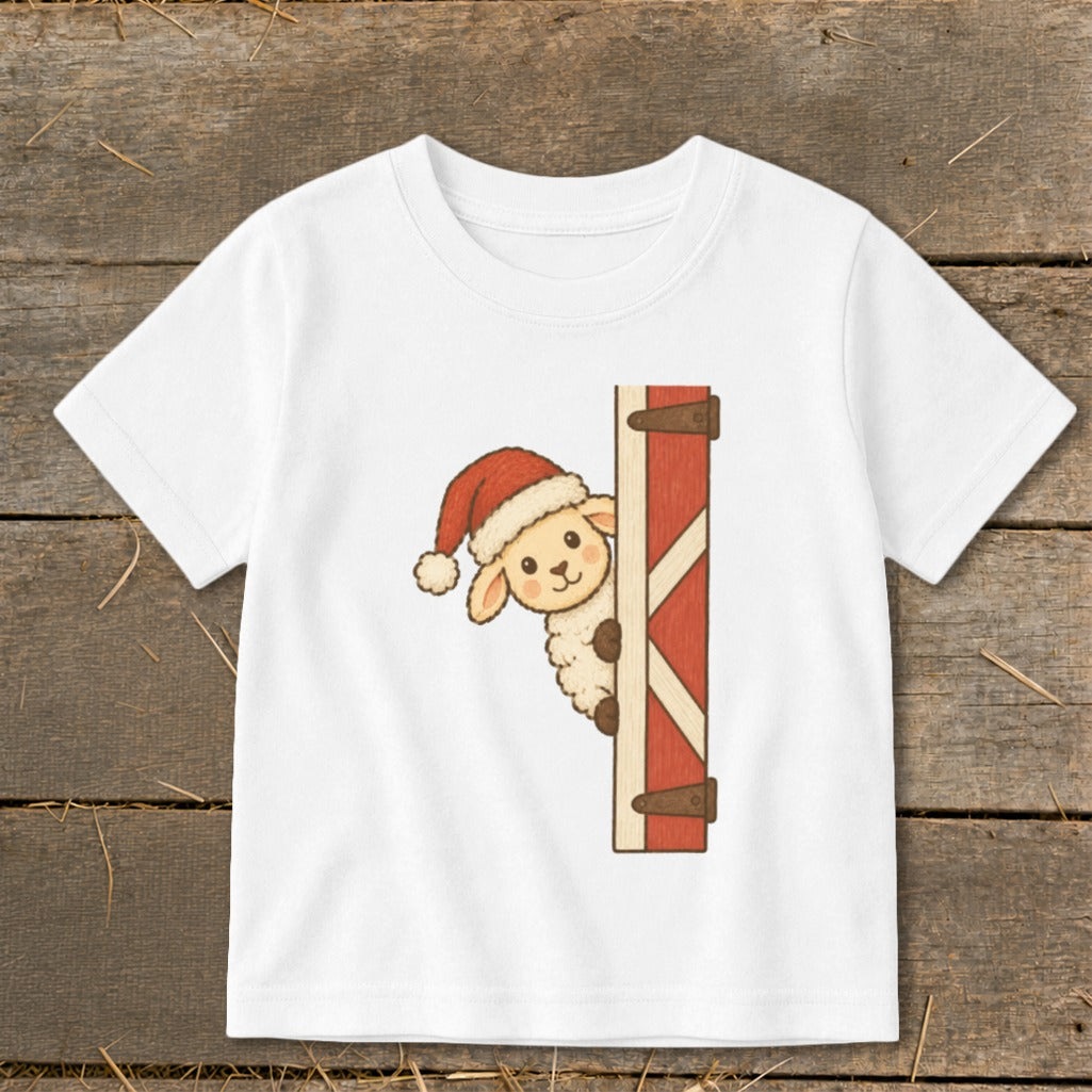 White t-shirt with a cartoon sheep wearing a Santa hat peeking from behind a red wooden door.