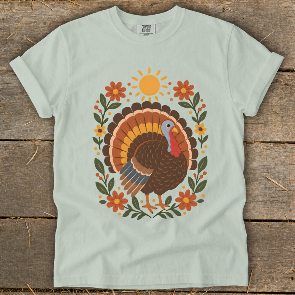 Light blue t-shirt with a Thanksgiving turkey surrounded by flowers and sun graphic.
