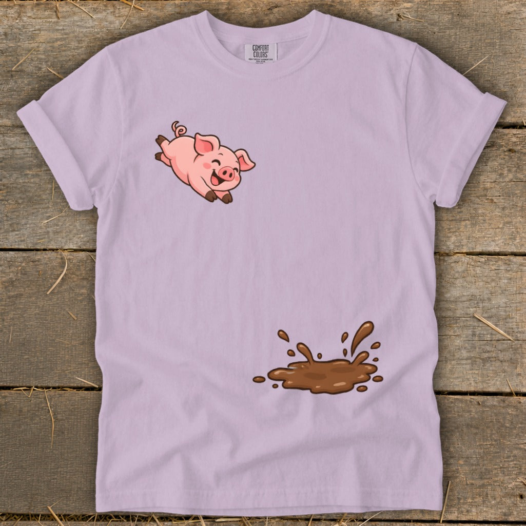 Pink pig leaping over a mud splatter on a light purple t-shirt.