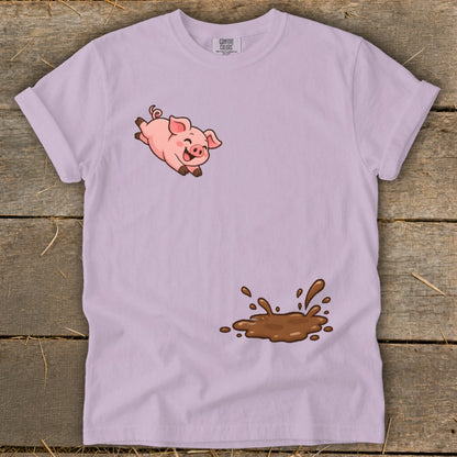 Pink pig leaping over a mud splatter on a light purple t-shirt.