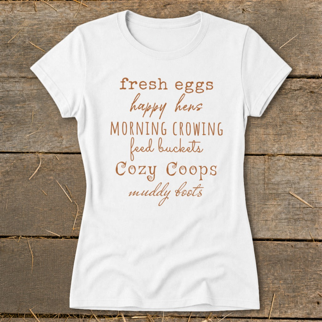 White t-shirt with text listing "fresh eggs happy hens MORNING CROWING feed buckets Cozy Coops muddy boots".