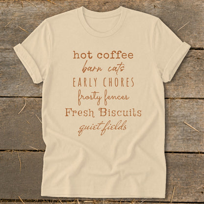 Light tan t-shirt with brown text listing "hot coffee, barn cats, early chores, frosty fences, Fresh Biscuits, quiet fields".