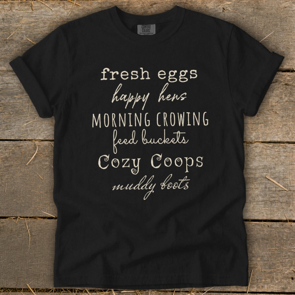 Black t-shirt with white text reading "fresh eggs happy hens MORNING CROWING feed buckets Cozy Coops muddy boots".
