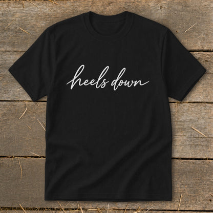 Black t-shirt with white script text that reads "heels down."