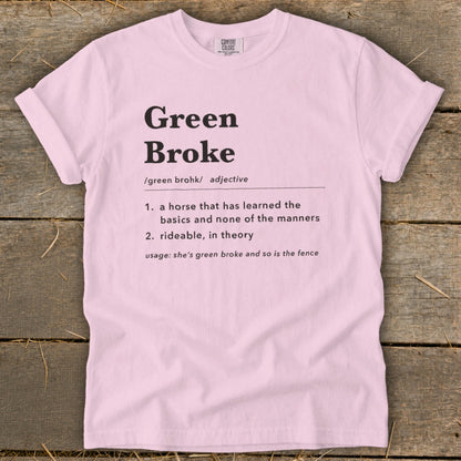 A pink t-shirt printed with a dictionary-style definition of Green Broke on a rustic wooden background.
