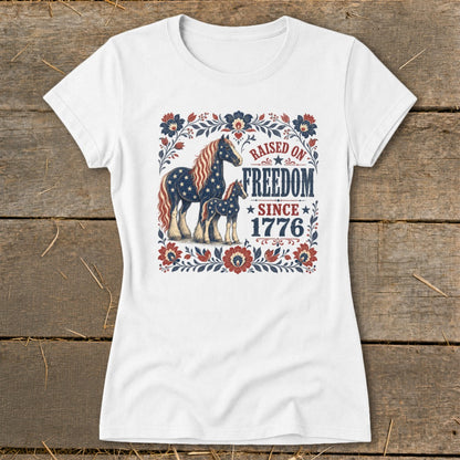White t-shirt with patriotic horses and "Raised on Freedom Since 1776" text.