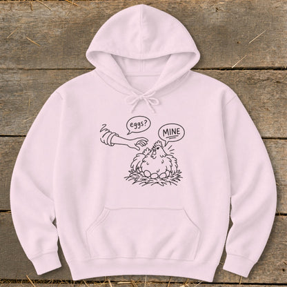 Light pink hoodie with a black line drawing of a hen on eggs saying "MINE" to a hand asking "eggs?".
