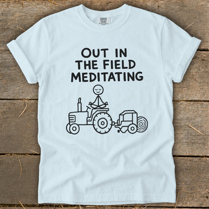 White t-shirt with black text and a drawing of a person meditating on a tractor.