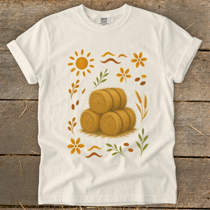 White t-shirt with fall harvest design featuring hay bales, sun, and leaves.