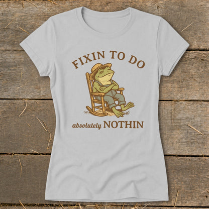 T-shirt with cartoon frog wearing a hat and overalls, relaxing in a rocking chair. Text reads "FIXIN TO DO absolutely NOTHIN".