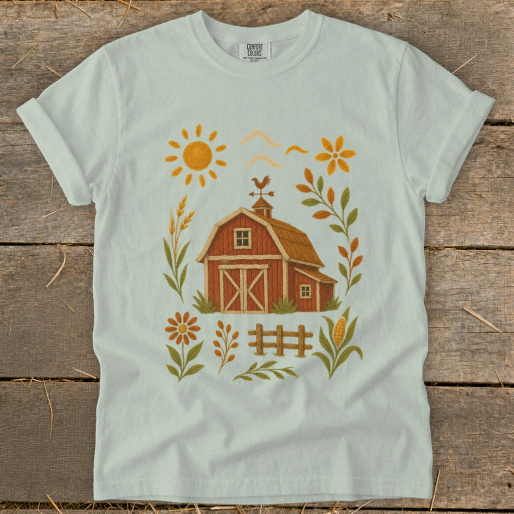 Light blue t-shirt with a farm scene graphic featuring a red barn, sun, flowers, and crops.