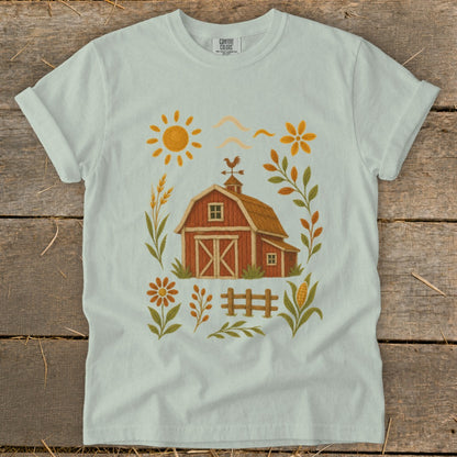 Light blue t-shirt with a farm scene graphic featuring a red barn, sun, flowers, and crops.