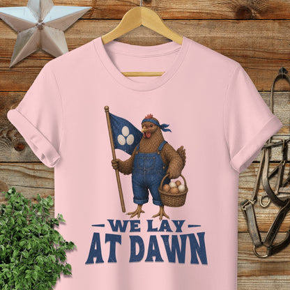 Pink t-shirt with a cartoon chicken holding a flag and basket, text "We Lay At Dawn."