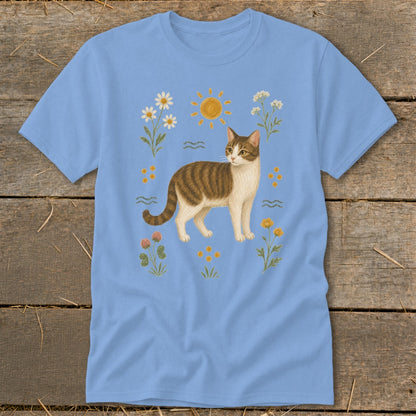 Light blue t-shirt featuring a tabby cat surrounded by flowers and a sun illustration.
