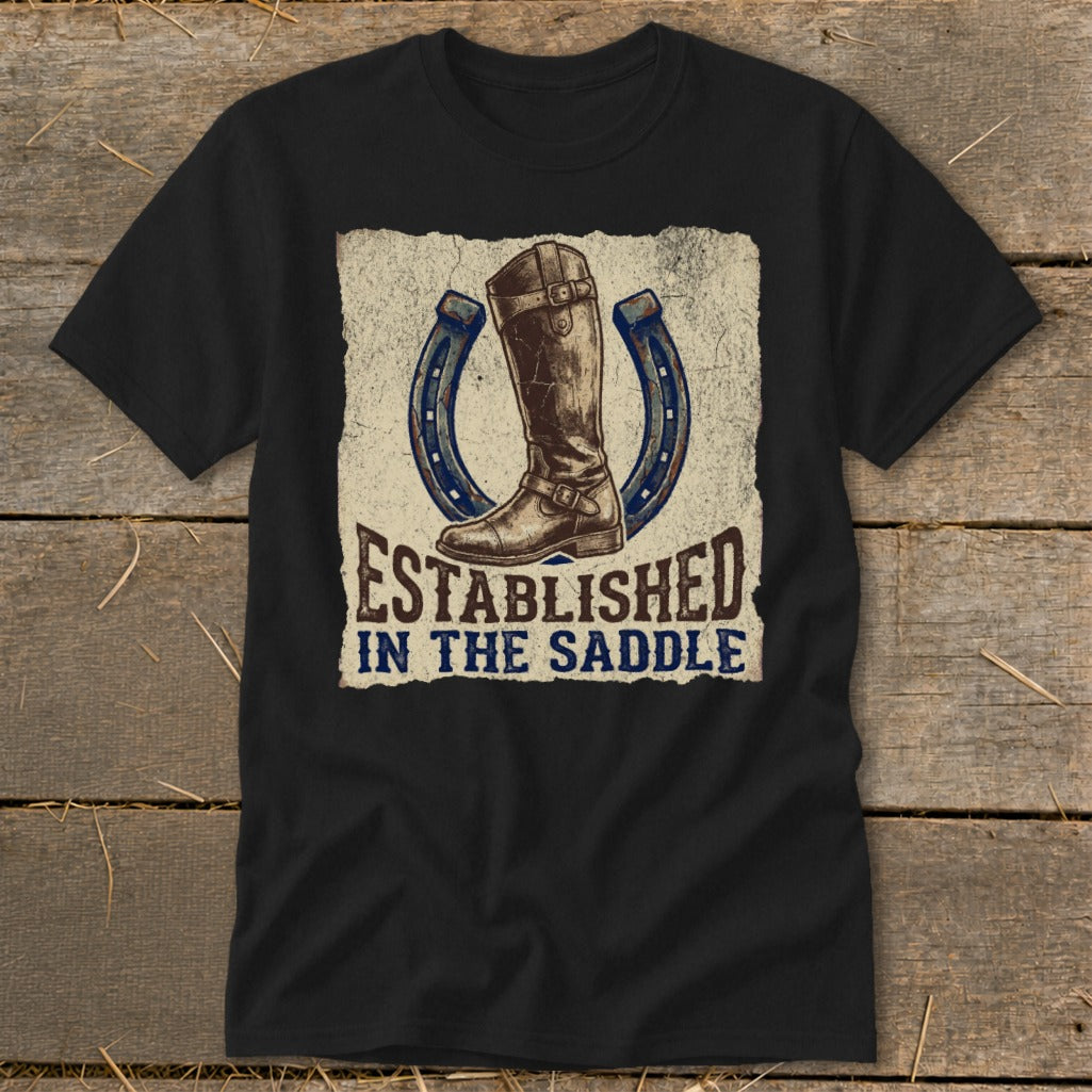 Black t-shirt with a graphic of a riding boot and horseshoes, reading "Established In The Saddle."