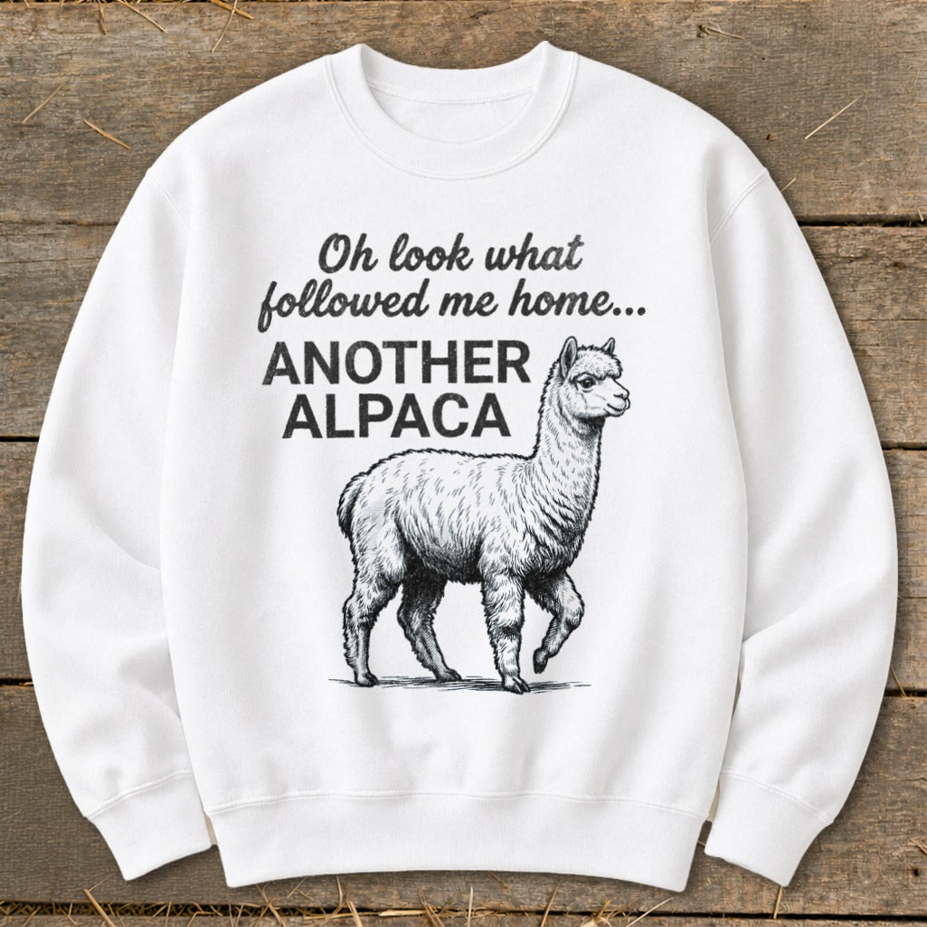 White sweatshirt with black text and alpaca illustration reading "Oh look what followed me home... ANOTHER ALPACA".