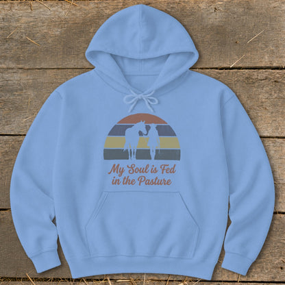 Light blue hoodie with graphic of horse, rider, and sunset; text: "My Soul is Fed in the Pasture".