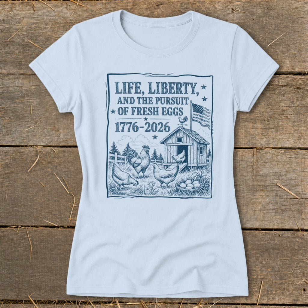 Light blue t-shirt with graphic of chickens, coop, and text "Life, Liberty, and the Pursuit of Fresh Eggs 1776-2026".