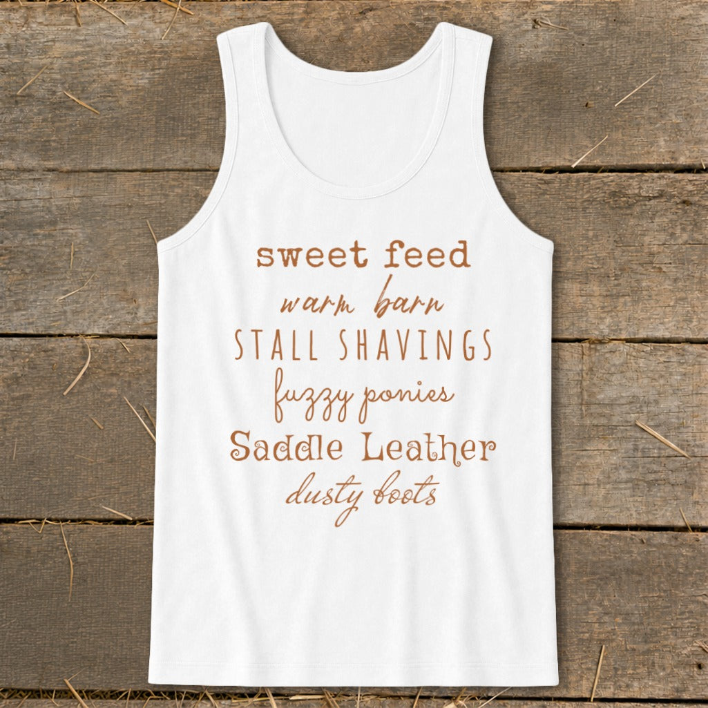 White tank top with text: sweet feed, warm barn, stall shavings, fuzzy ponies, saddle leather, dusty boots.