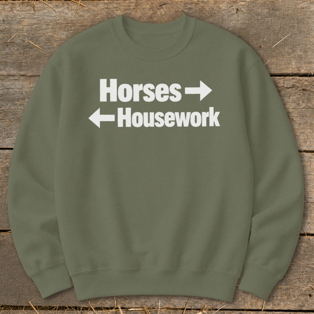 An olive green crewneck sweatshirt featuring white text that reads Horses with a right-pointing arrow and Housework with a left-pointing arrow.
