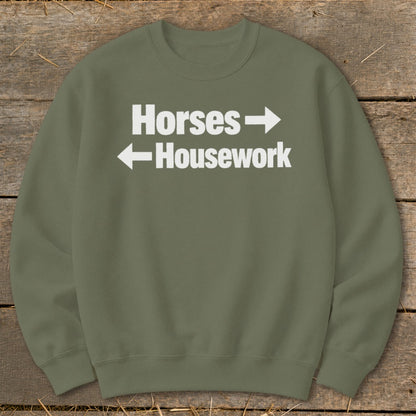 An olive green crewneck sweatshirt featuring white text that reads Horses with a right-pointing arrow and Housework with a left-pointing arrow.