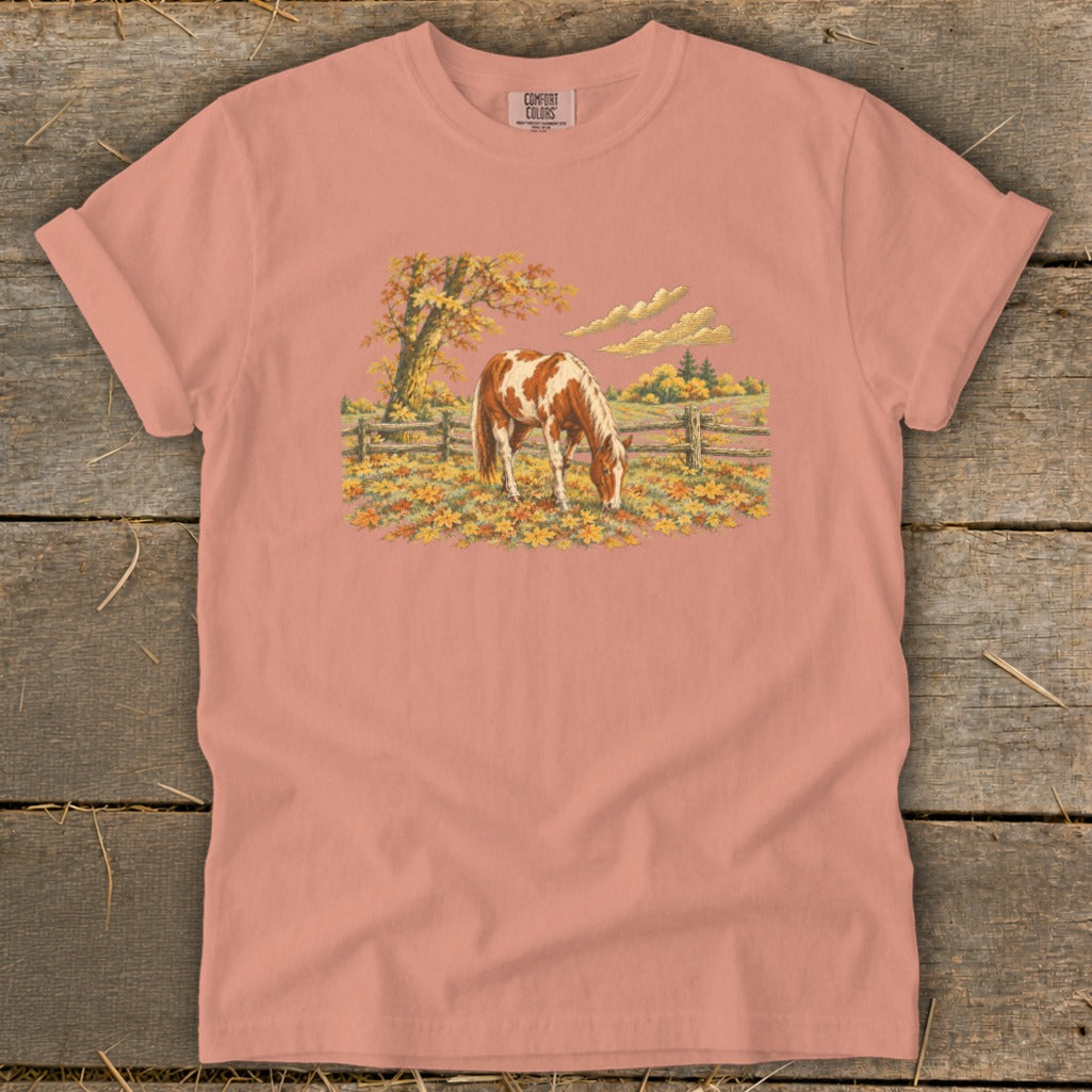 Peach t-shirt with a painted brown and white horse grazing in an autumn field.