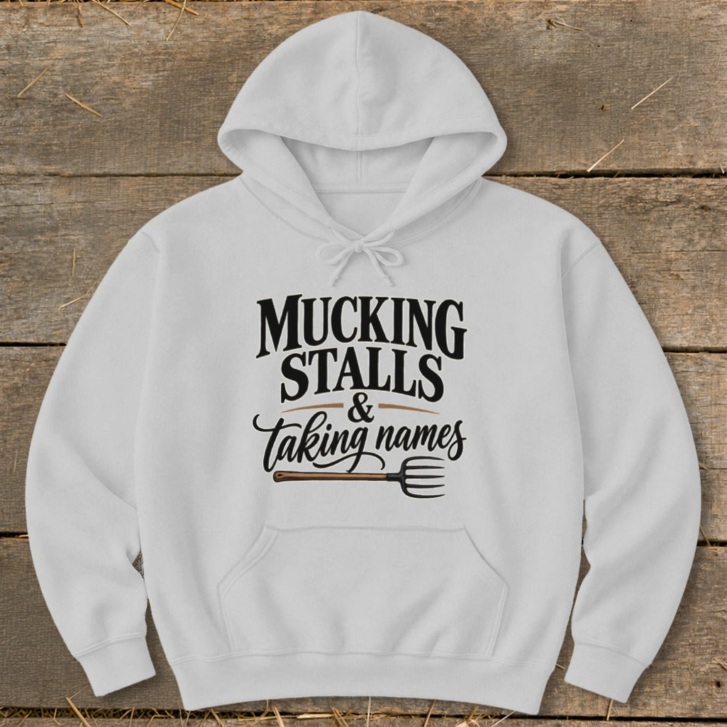 White hoodie with "MUCKING STALLS & taking names" text and a pitchfork graphic.