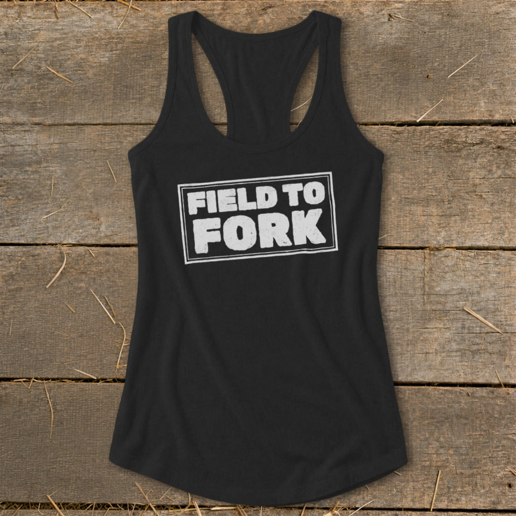 A black racerback tank top featuring the text Field to Fork in white on a rustic wooden background.