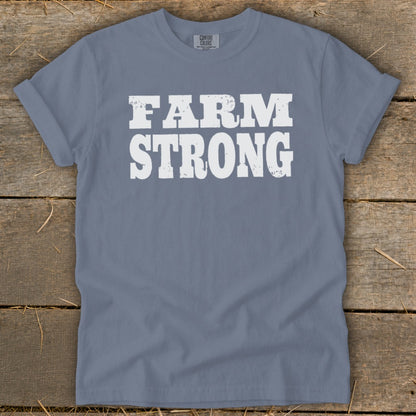 A grey t-shirt featuring the white distressed text FARM STRONG laid flat on a rustic wooden background.