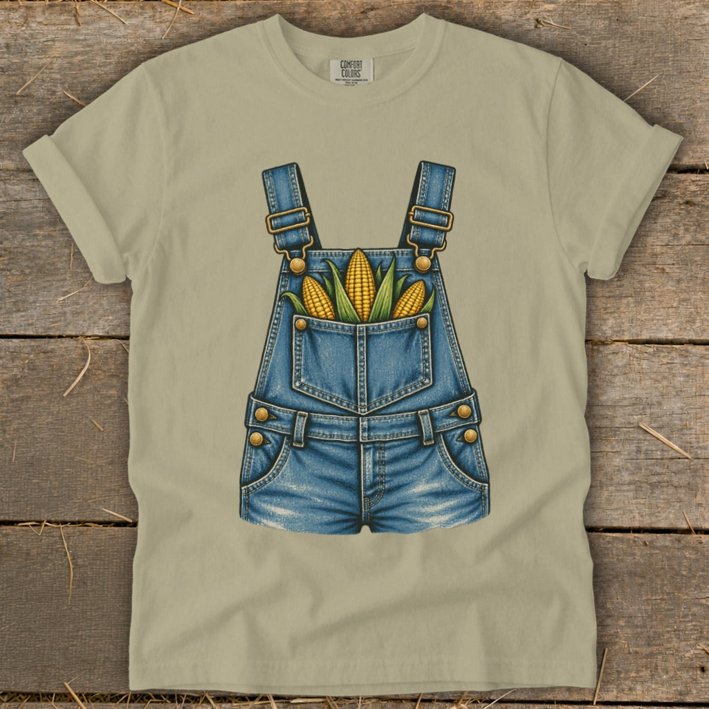 Tan t-shirt featuring denim overalls with corn in the pocket.