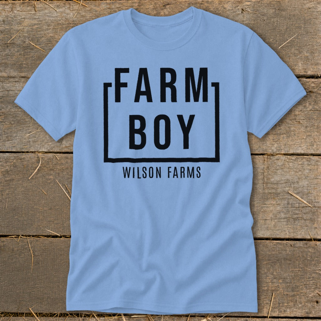 Light blue t-shirt with black text "FARM BOY WILSON FARMS" inside a black square.