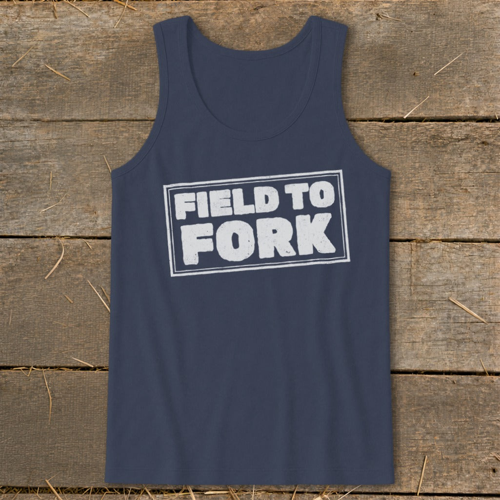 Dark blue tank top featuring the white text FIELD TO FORK inside a distressed rectangular box, laid flat on a rustic wooden background.