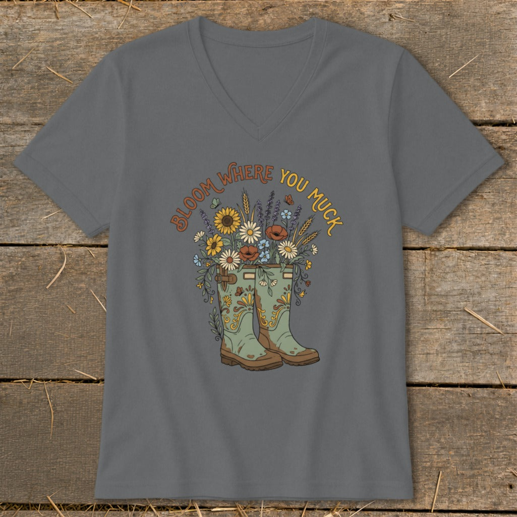 Gray v-neck shirt with "Bloom Where You Muck" text over cowboy boots and flowers.