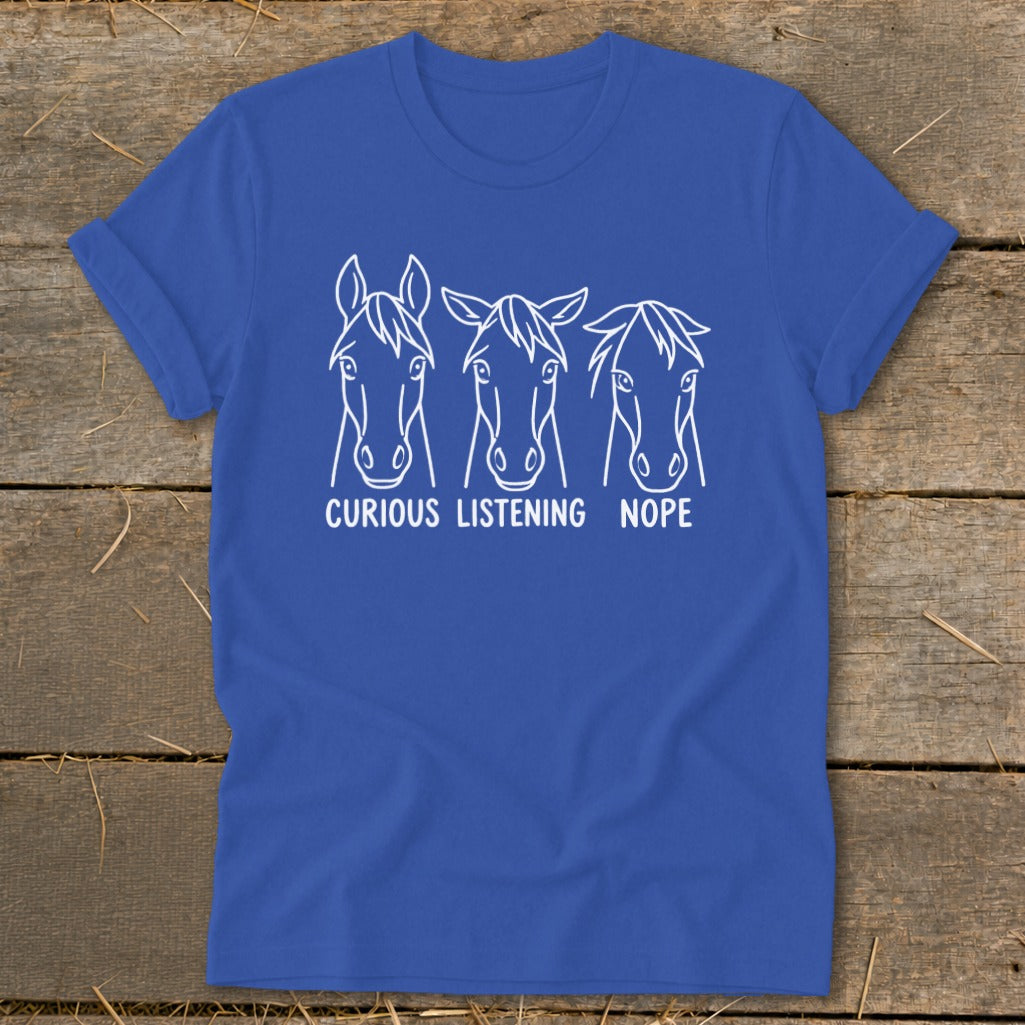 A blue t-shirt featuring a white graphic of three horse heads labeled Curious, Listening, and Nope.