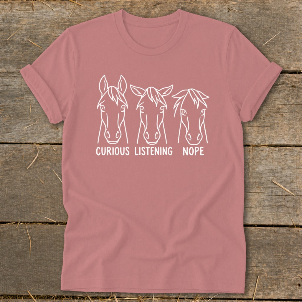 Dusty pink t-shirt featuring three white horse head line drawings with the text Curious, Listening, and Nope.