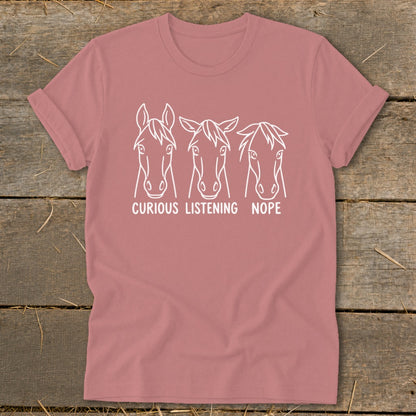 Dusty pink t-shirt featuring three white horse head line drawings with the text Curious, Listening, and Nope.