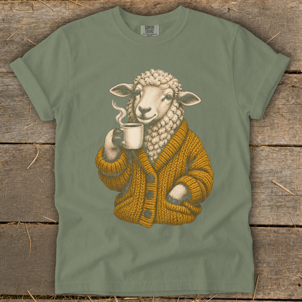 Sage green t-shirt featuring a graphic of a sheep wearing an orange cardigan and holding a steaming mug.