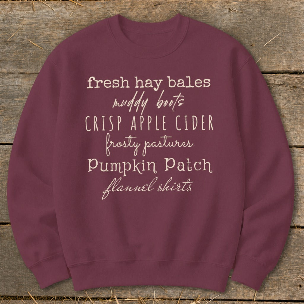 Burgundy sweatshirt with white text listing fall themes: fresh hay bales, muddy boots, crisp apple cider, frosty pastures, pumpkin patch, flannel shirts.