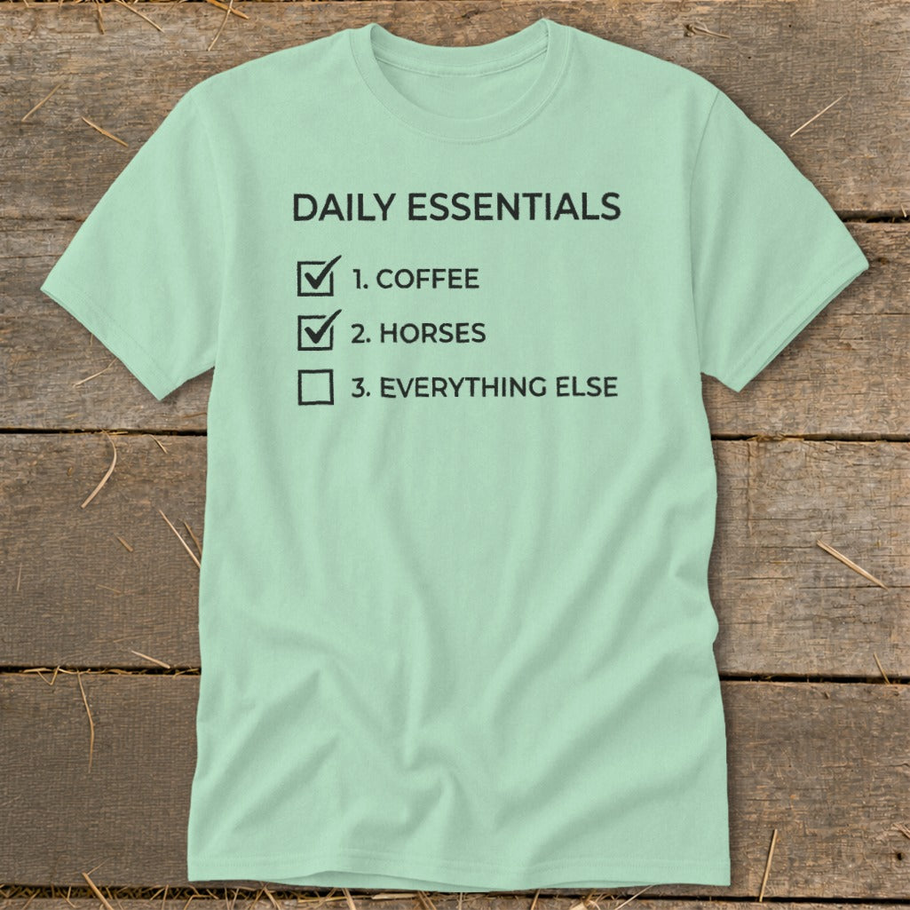 Light green t-shirt with black text listing "Daily Essentials: 1. Coffee, 2. Horses, 3. Everything Else".