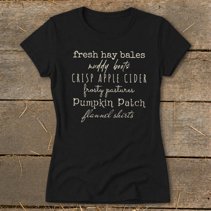 Black t-shirt with white text listing fall themes: fresh hay bales, muddy boots, crisp apple cider, frosty pastures, pumpkin patch, flannel shirts.